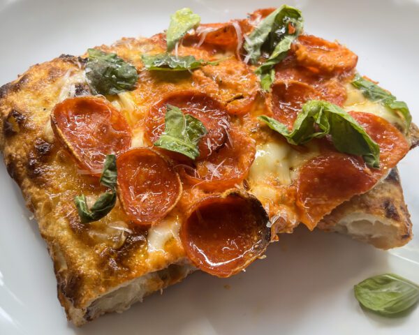 Slice of pizza with vodka sauce, pepperoni, and basil